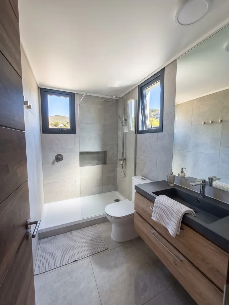Baño con ducha, ventana y mueble de lavamanos de madera